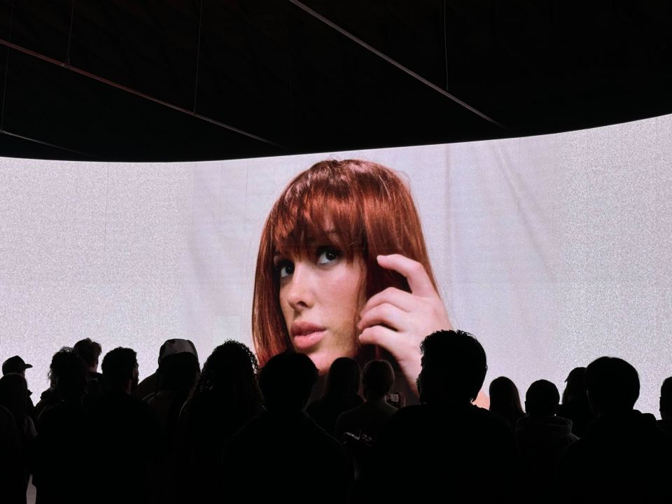 Audience watching a large screen showing a woman with red hair.